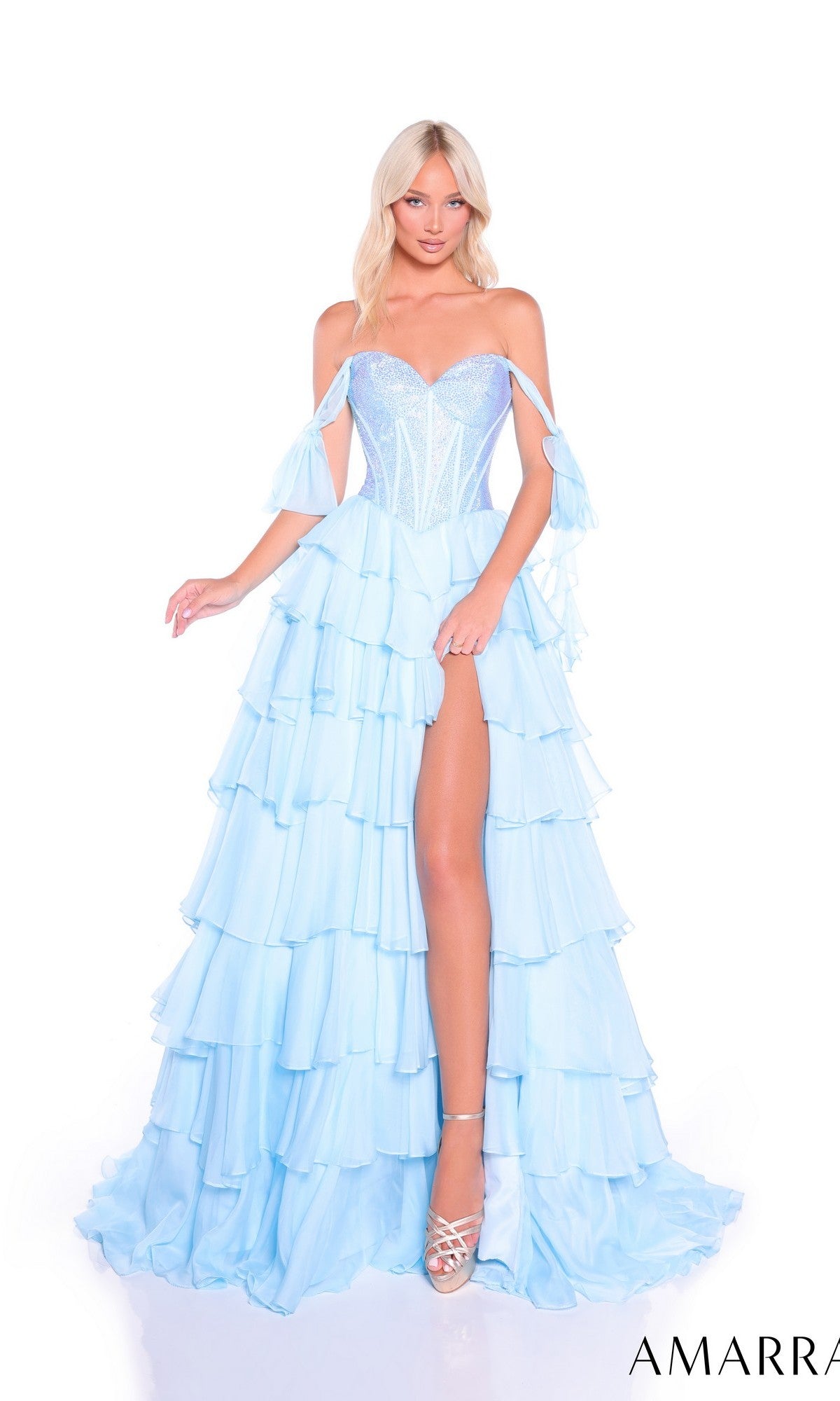 A woman in the Amarra 89285 long prom dress, featuring a light blue off-the-shoulder design, tiered chiffon skirt, and thigh-high slit, pairs it with silver high heels while standing against a white background.